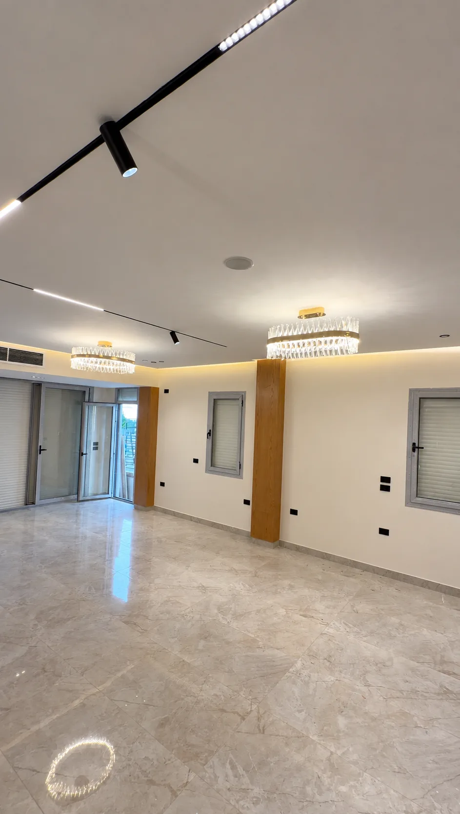 An open reception hall with two crystal chandeliers, track lights and tall windows.