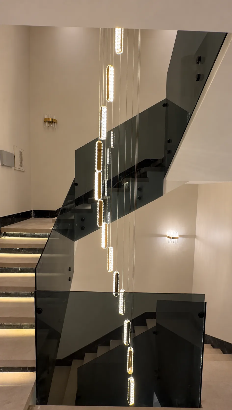 A cascading chandelier of lit links hanging through the stairwell, beside the glass balustrade.