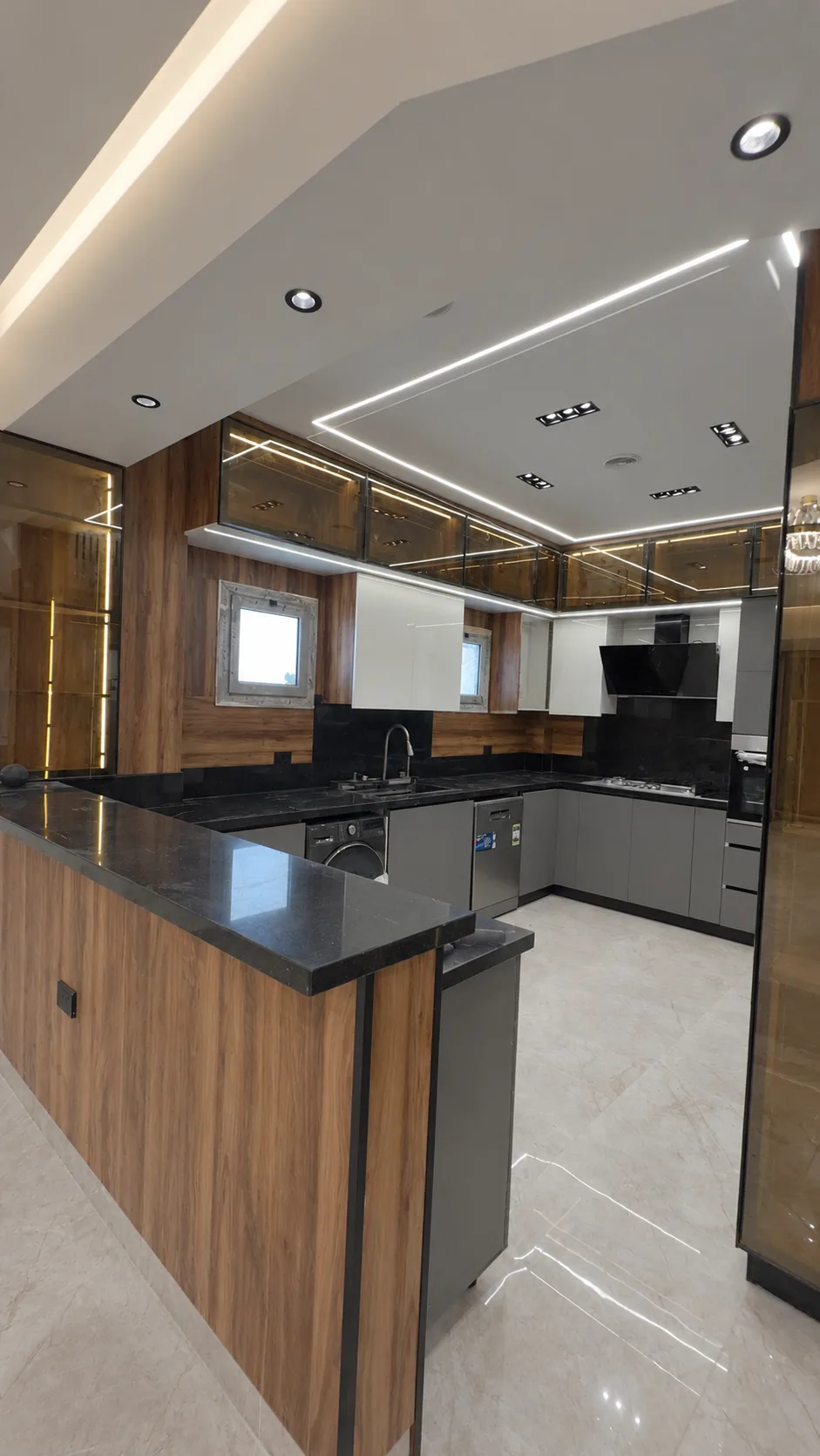 Along the wood-faced kitchen island towards the window, with lit cabinets above.