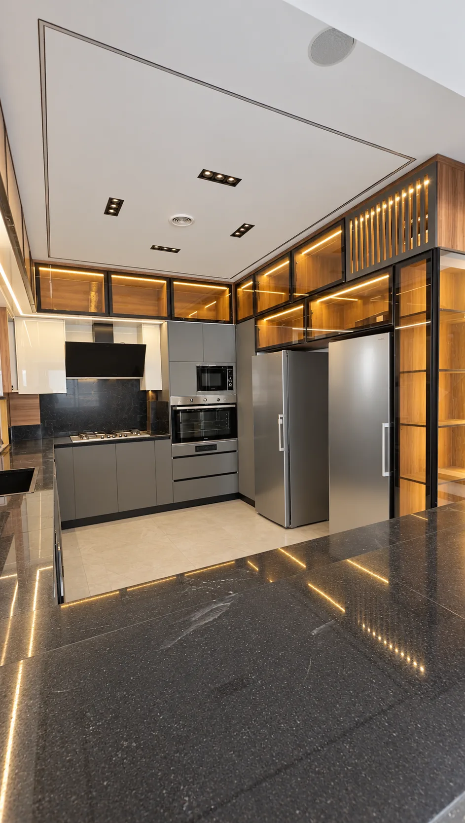 The kitchen: tall glass display cabinets lit from within, built-in appliances and a dark stone island with lines of light.