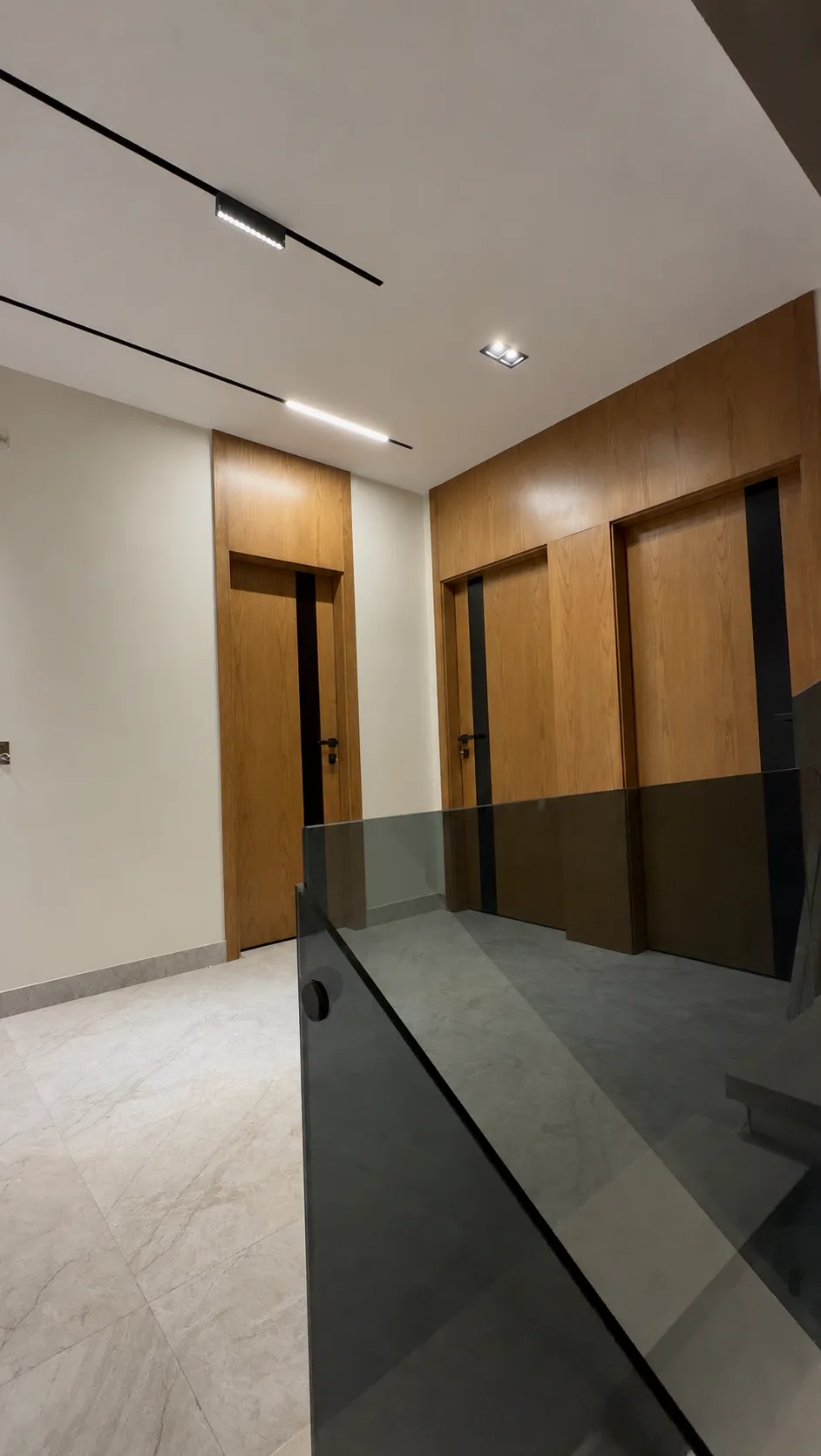 An upper hall with wood-clad doors, track lights and the glass balustrade of the stairs.