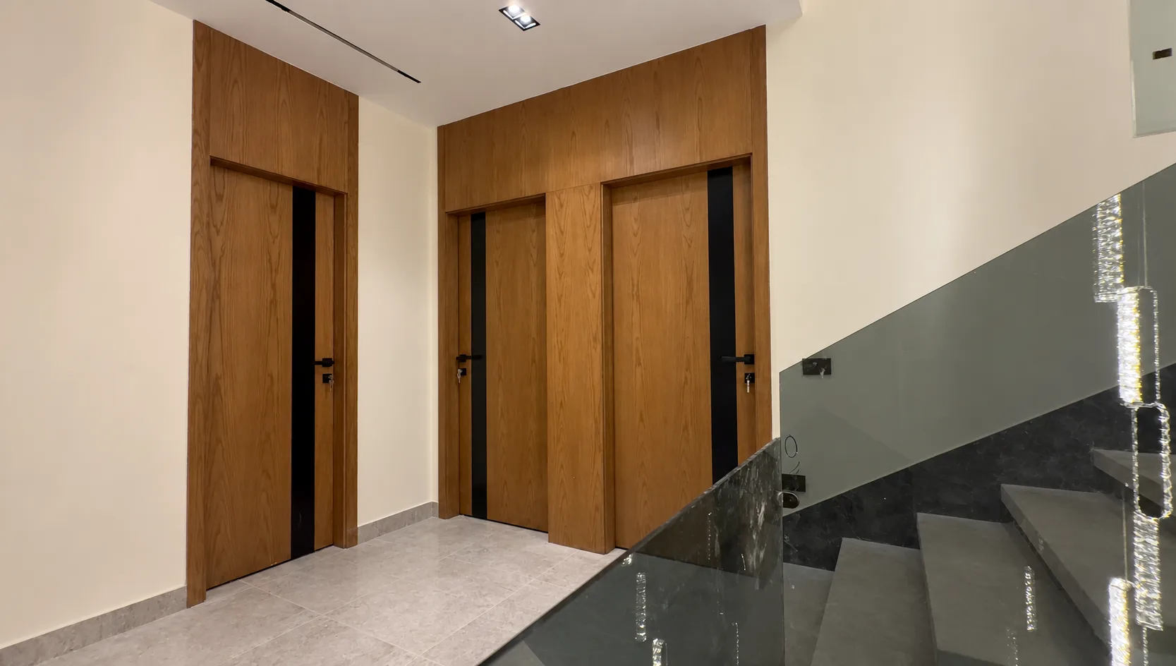 Tall wood doors with black inlays on the landing, beside the glass balustrade of the stairs.
