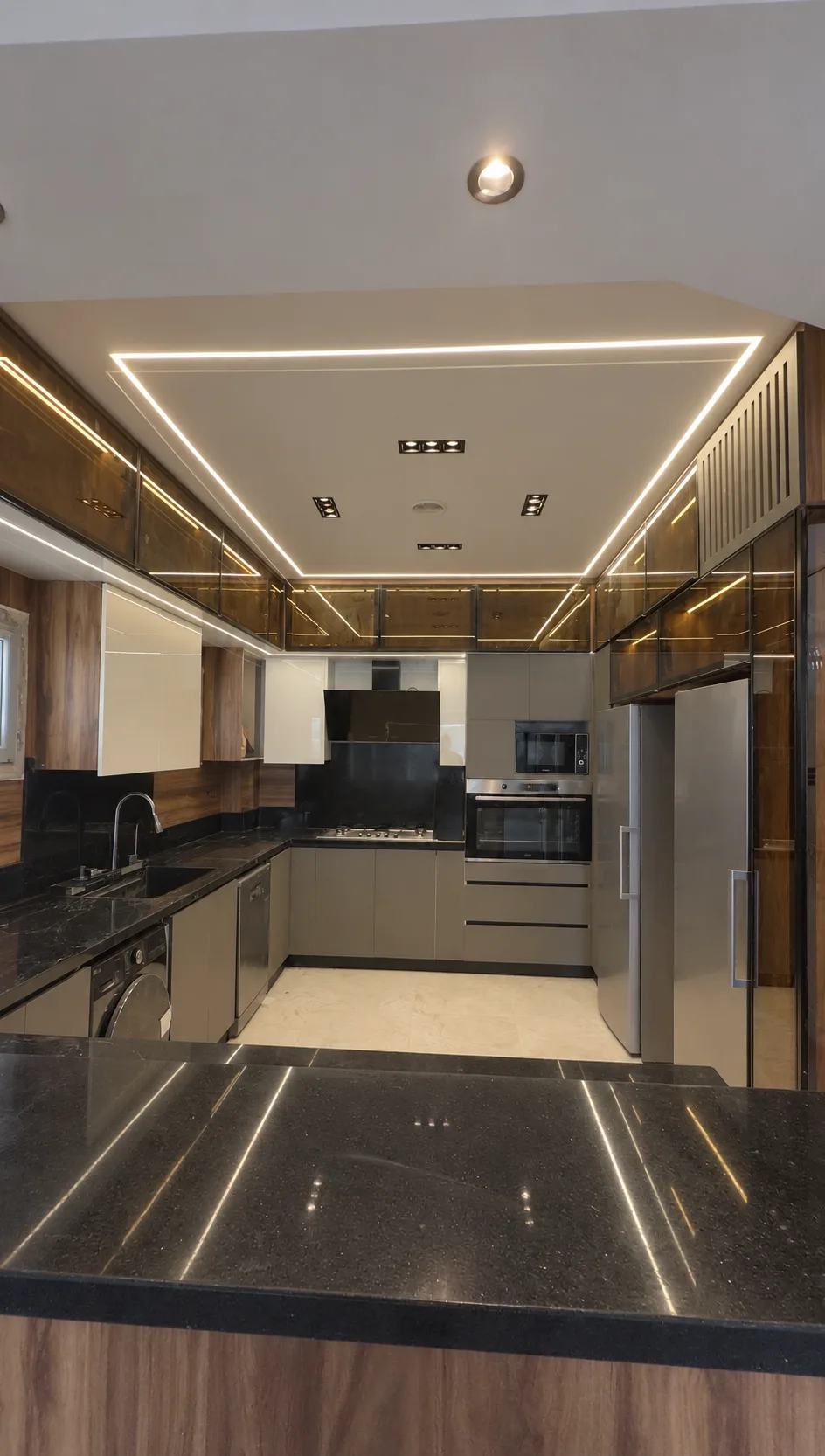 The kitchen island with lines of light reflected in its dark stone top, under a lit frame in the ceiling.