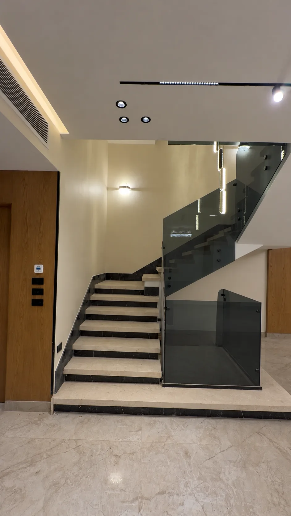 The staircase from the ground floor: light stone steps, a glass balustrade and pendant lights.